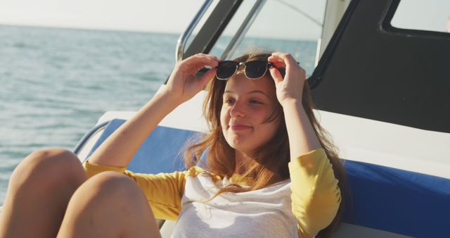 Happy caucasian teenage girl raising sunglasses and smiling on deck of small boat on a sunny day. Leisure, hobbies, free time, travel and vacations.