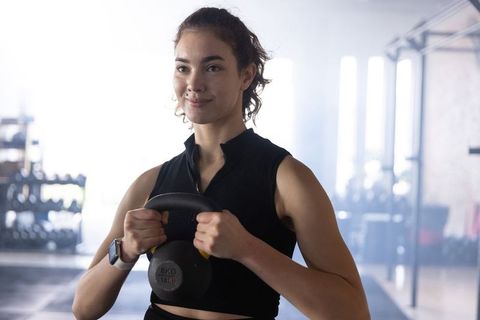 Determined young woman lifting kettlebell during strength training in bright gym