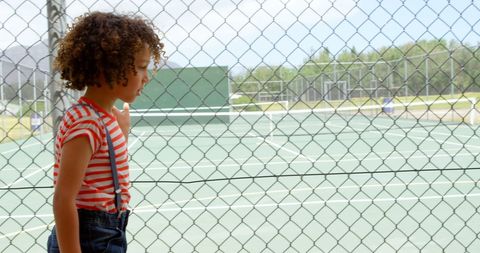 Child standing by tennis court fencing during sunny day - Download Free Stock Images Pikwizard.com