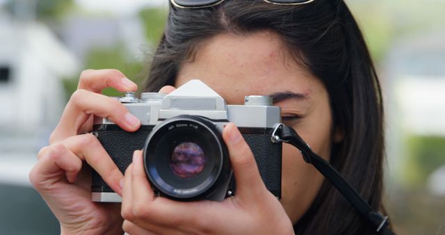 A young Caucasian woman is focusing a vintage camera to take a photograph, with copy space. Her eye is pressed against the viewfinder, capturing the essence of a photography enthusiast in action.