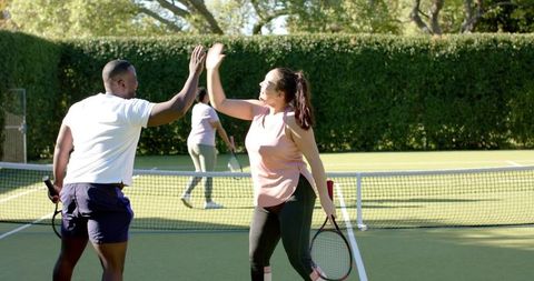 Diverse Friends Celebrate on Tennis Court with High Five