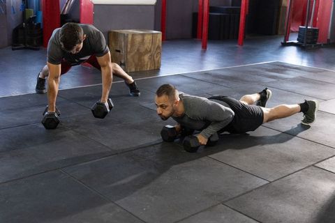 Partners performing dumbbell plank push-ups and renegade rows on gym floor for strength