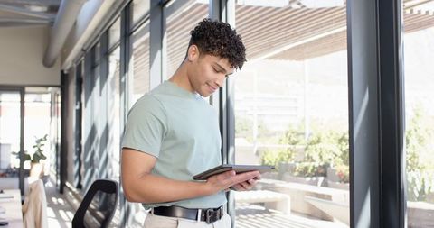 Young Professional Using Tablet Near Modern Office Windows