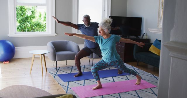 Senior couple practicing yoga together in their living room. Man and woman posing in yoga attire, doing stretching exercises on yoga mats. Ideal for concepts related to fitness for seniors, healthy aging, indoor activities, and couples' exercises.