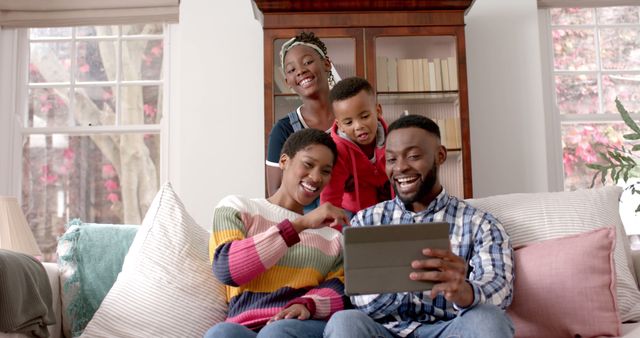 This heartwarming image of an African American family happily engaging with a tablet together perfectly suits advertisements and content related to family time, technology in daily life, or cozy home settings. It beautifully captures the essence of love and connection within a family, making it ideal for parenting blogs, family product promotions, or digital connectivity-themed marketing.