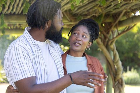 Couple sharing conversation under sunlit garden pergola, affectionate outdoor moment