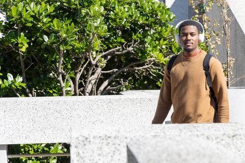 African american student walking on sunlit campus terrace with headphones and backpack