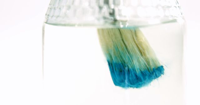 Close-up image shows paintbrush submerged in water, with blue paint dissolving. Useful for illustrating art supplies, creative processes, or blog articles about painting techniques. Great for art tutorials, artist promotions, or hobby-related websites.