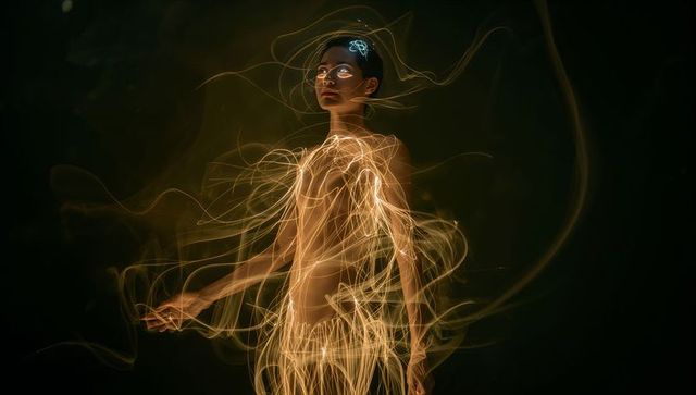 Ethereal female model wrapped in golden light trails with luminous halo and glowing ribbons