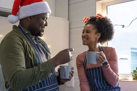 African american couple wearing santa hat and aprons enjoying cozy holiday coffee in sunlit kitchen