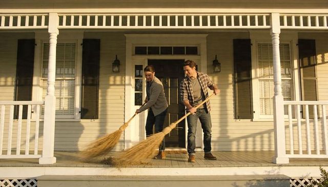 Young couple sweeping wooden front porch during golden hour, teamwork home care