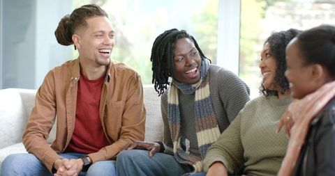 Diverse friends laughing and chatting on sofa in cozy daylight living room
