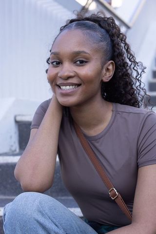 Smiling african woman in her twenties sitting on urban steps leaning with crossbody strap