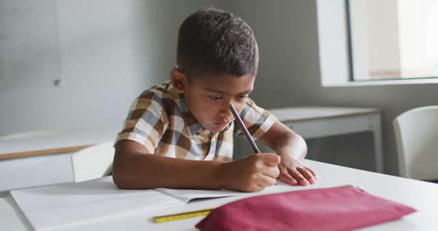 Image of focused biracial boy sitting at desk in classroom. primary school education and learning concept.