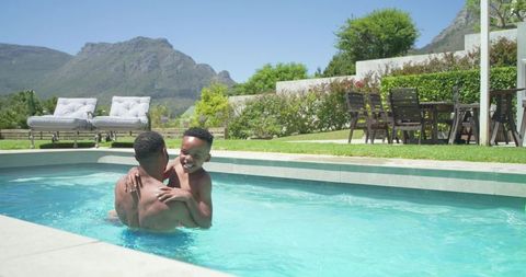 Father lifting son in sunny backyard pool with mountain view, family bonding