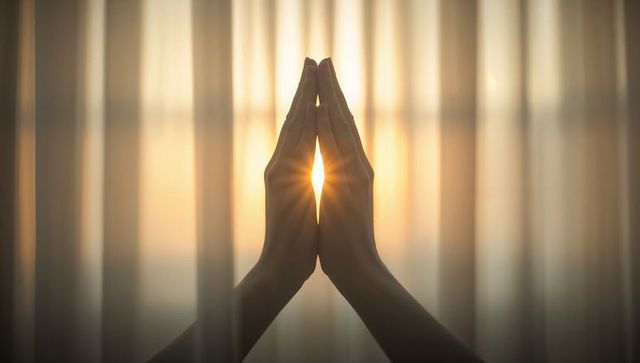 Pressing hands together at window with sunburst flare, meditation mindfulness calm morning