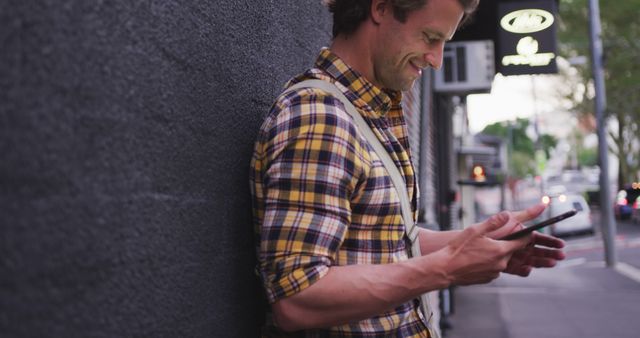 Smiling Man Leaning Against Wall Using Smartphone on City Sidewalk - Download Free Stock Images Pikwizard.com