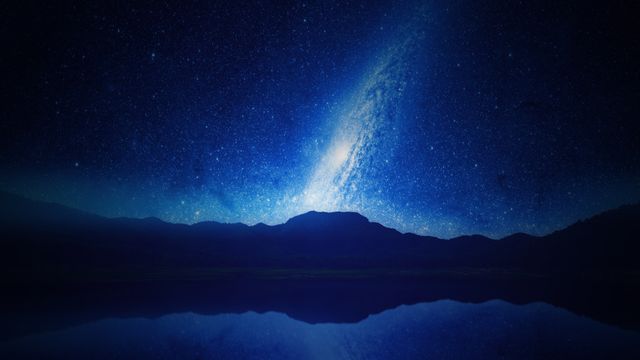 Capturing night sky illuminated by millions of stars with Milky Way stretching over silhouetted mountain range. Darkened foreground shows calm lake reflecting sky, adding symmetry. Can be used for backgrounds, nature-related content, astronomy-themed projects, and creating a peaceful, serene atmosphere.