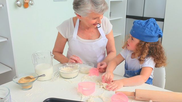 Warm image capturing a grandmother and granddaughter joyfully baking in a sunlit kitchen. The scene showcases the child-like creativity and guidance from the vigilant grandmother, offering a heartwarming view into familial love and shared activities. Ideal for representing families, cookbooks, culinary advertisements promoting wholesome family fun, or educational content on learning through play and bonding experiences.