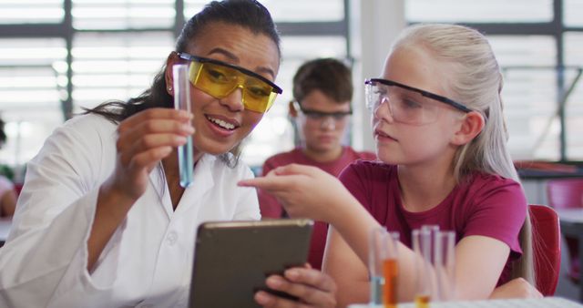 Diverse female teacher and schoolgirl wearing protective glasses with test-tube on chemistry class. children at primary school.