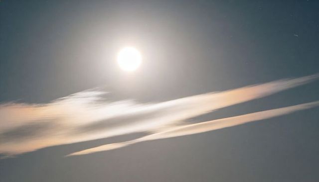 Full moon halo casting soft lunar glow over wispy clouds and faint stars