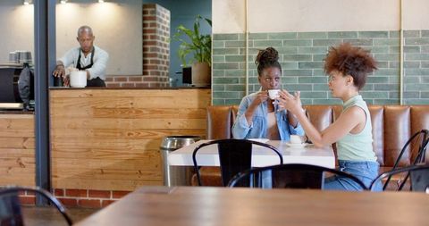 African American women chatting and sipping coffee in cozy rustic cafe interior