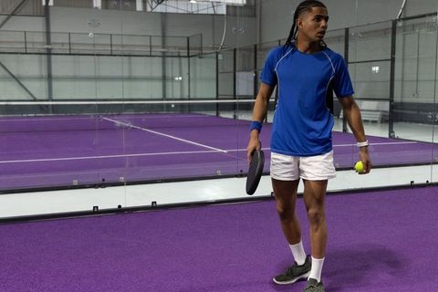 African american padel player standing on purple court holding paddle and ball