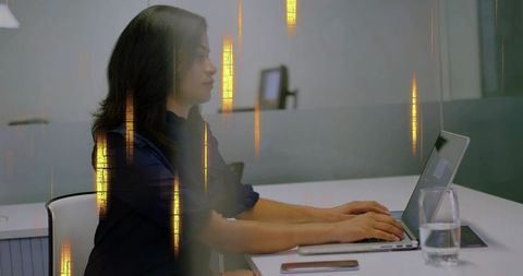Focused professional woman typing on laptop in minimalist office with glass partition