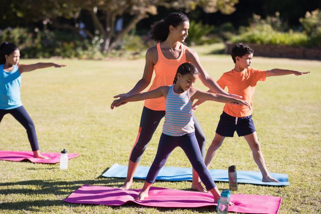 Female instructor guiding children in yoga poses in a park. Ideal for promoting outdoor fitness, family activities, and healthy lifestyles. Suitable for use in wellness blogs, fitness programs, and educational materials about yoga for kids.