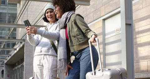 Diverse friends traveling together checking phone and laughing with luggage at terminal