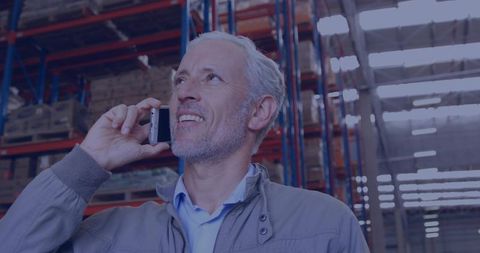 Senior warehouse supervisor using smartphone while inspecting racking and inventory