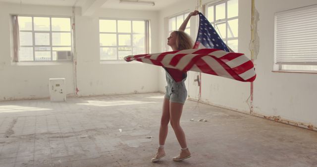 Depicting a young woman celebrating freedom and patriotism, this image is perfect for projects about independence, American spirit, or youth culture. The setting in an empty, abandoned building adds a unique and stark contrast, highlighting resilience and the pursuit of happiness. Ideal for use in advertisements, social media posts, and blogs focused on themes of patriotism, independence and youthful exuberance.
