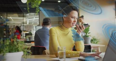 Remote work multitasking: woman speaking into smartphone while typing on laptop in coworking hub