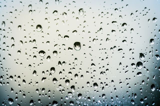 Raindrops cling to window glass creating a beautiful pattern of water droplets with a blurred background. Ideal for use in designs related to weather, nature, and atmosphere. Perfect for blogs, websites, and advertising campaigns focusing on rainy days, mood, and reflections.