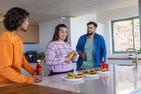 Diverse friends assembling burgers at kitchen island with condiments and drinks