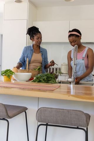 African american mom and teen daughter preparing healthy meal together in modern kitchen