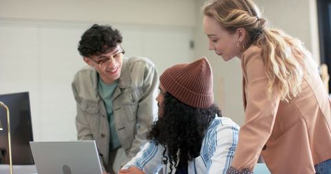 Diverse team collaborating over laptop in modern office meeting, casual business attire