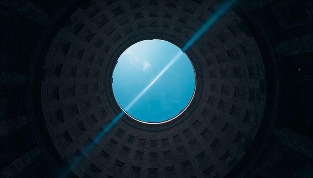 Circular oculus framing bright blue sky with sunbeam through classical dome geometry