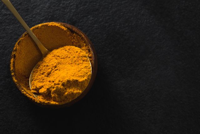 Close-up view of vibrant turmeric powder in a wooden bowl on a dark background. Ideal for use in culinary blogs, healthy eating articles, spice and herb websites, and cooking magazines. Perfect for illustrating recipes, natural remedies, and organic food products.