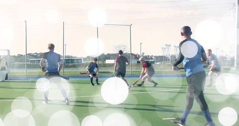 Male field hockey players competing on turf with sun flare and bokeh light effects