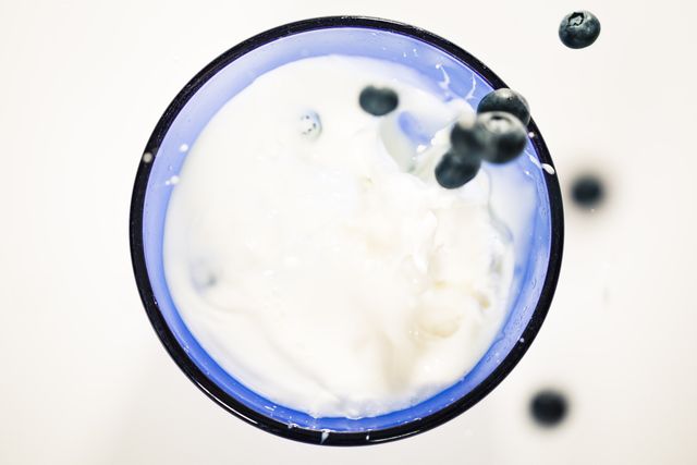 Blueberries are splashing into yoghurt in a blue bowl, with a focus on the motion and freshness. Perfect for health-related articles, food blogs, or breakfast recipe illustrations.
