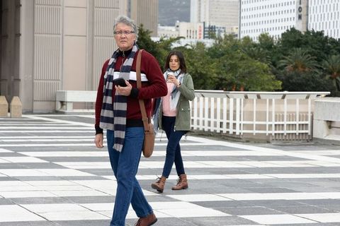 Senior man walking on checkerboard plaza while woman sipping coffee and checking phone