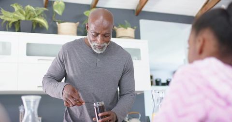 Mature man preparing morning drink in home kitchen while child watching at countertop
