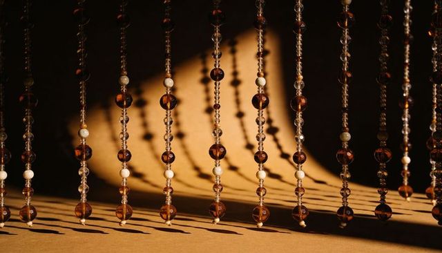 Amber and crystal bead curtain casting long dramatic shadows on warm textured backdrop