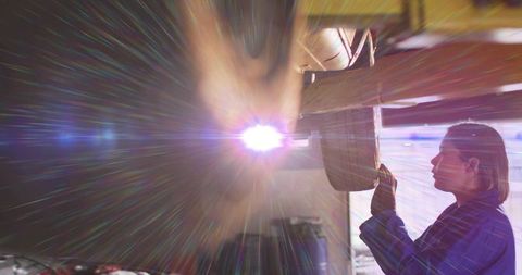 Female technician inspecting raised car wheel well under dramatic lens flare