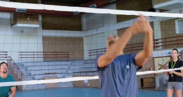 Young individuals engaged in an active game of volleyball inside a gymnasium. This is an ideal visual for promoting health, fitness, team sports, recreational activities, and training programs. Suitable for websites, advertisements, articles on sports and exercise, or educational materials.