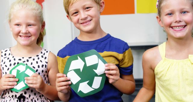 Smiling caucasian elementary schoolboy and schoolgirls holding recycling symbols in classroom. Recycling, ecology, education, childhood, learning and school, unaltered.