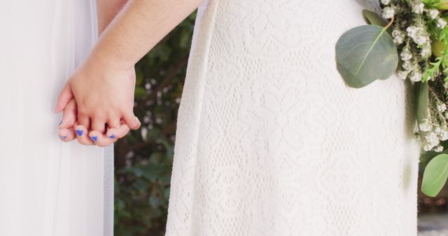 Close-up view of a bride holding hands with her partner on their wedding day, showcasing her blue nail polish and lace wedding dress. Ideal for use in wedding-themed content, marriage celebrations, and romantic settings.