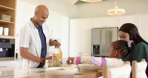 Diverse family enjoying bright modern kitchen breakfast together with father pouring juice