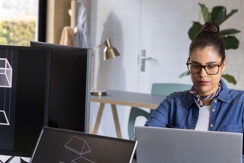 Creative professional working on laptop with dual monitors in modern minimalist studio